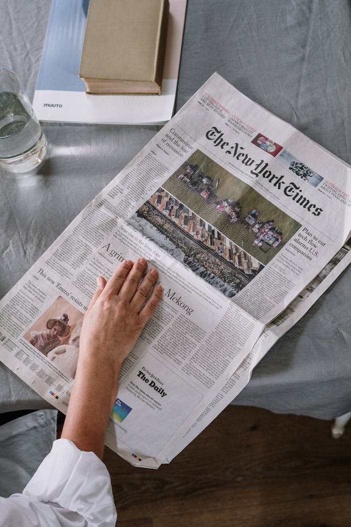 digital Person reading The New York Times at home with books and glass of water on the table.