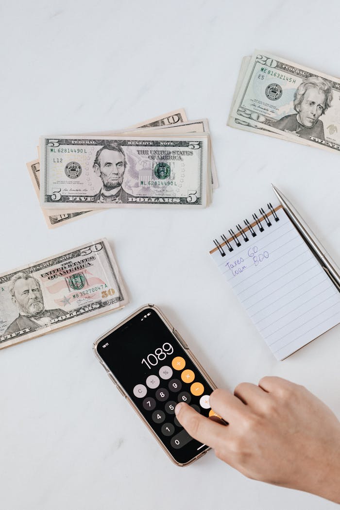 why-choose-us Overhead view of a hand using a calculator with US dollars and notes, representing finance and budgeting.